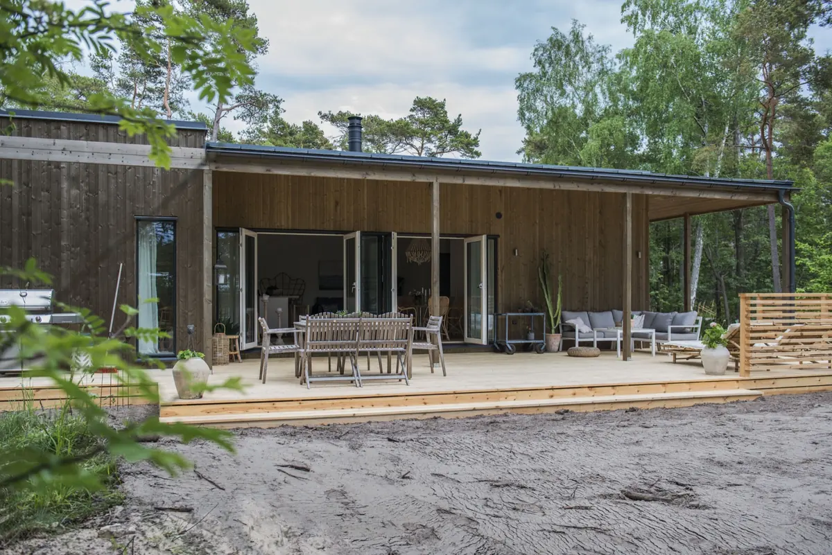 Tofta 100 bland tallarna, med altanen under det utfällda taket och glasdörrarna öppna