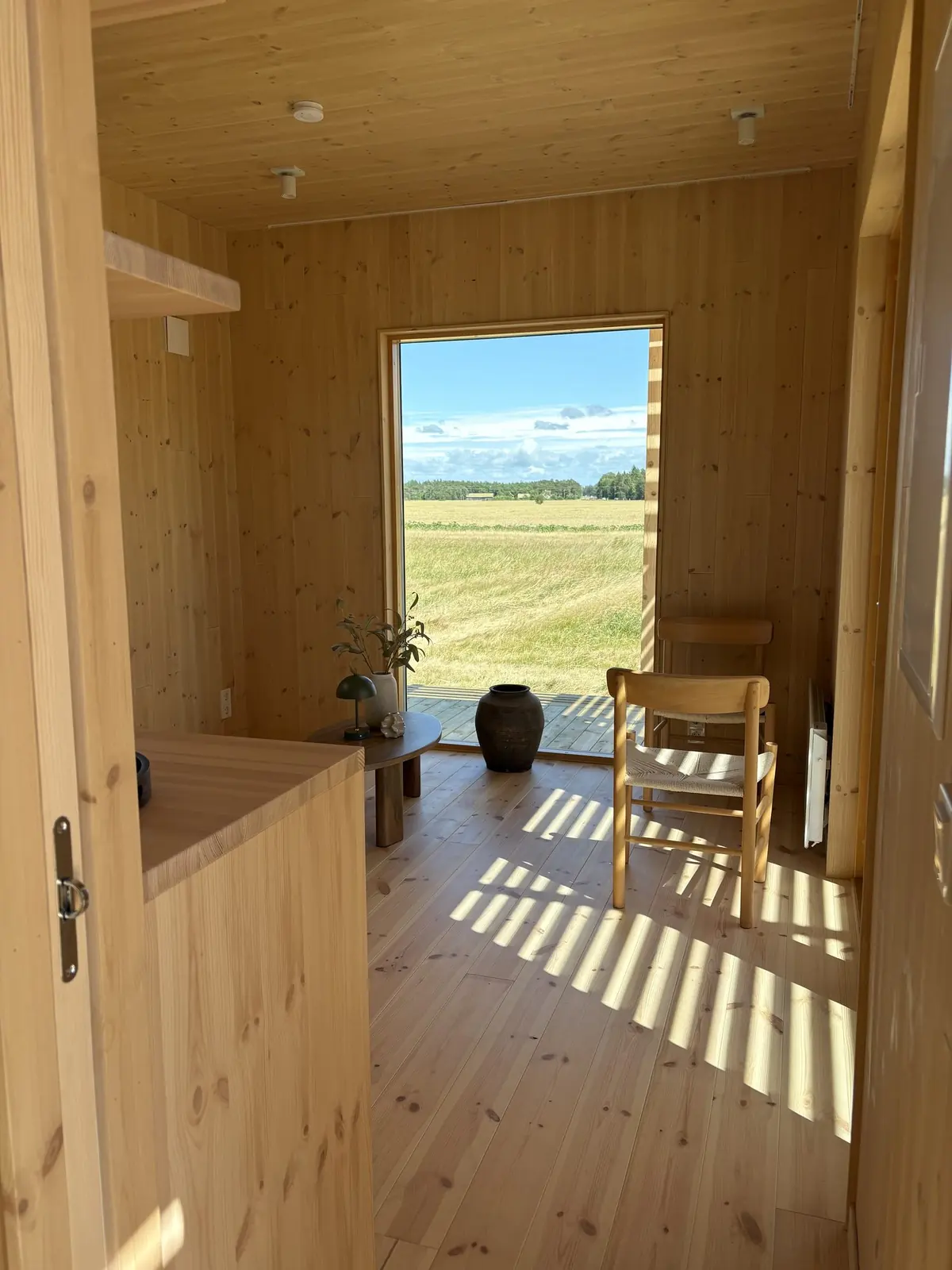 Allrummet i visningshuset, ett Nära Naturen 30, med öppen dörr ut mot åkern och solljus genom spaljén