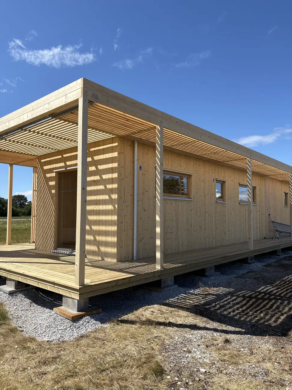 Långsidan på visningshuset i Visby, ett Nära Naturen 30, med entrédörr, fönster och altanen under pergolan