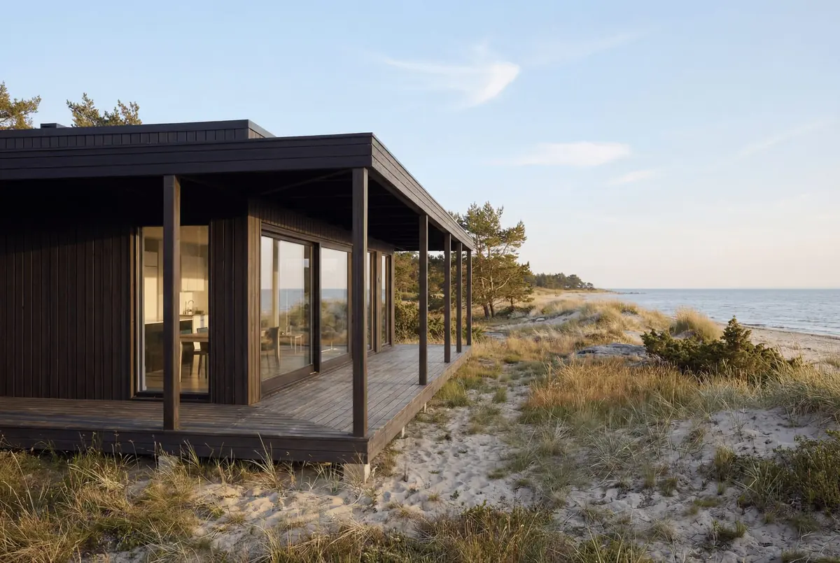 Visualisering: Tofta 50 i mörk panel med tak över verandan, bland dyner vid havet